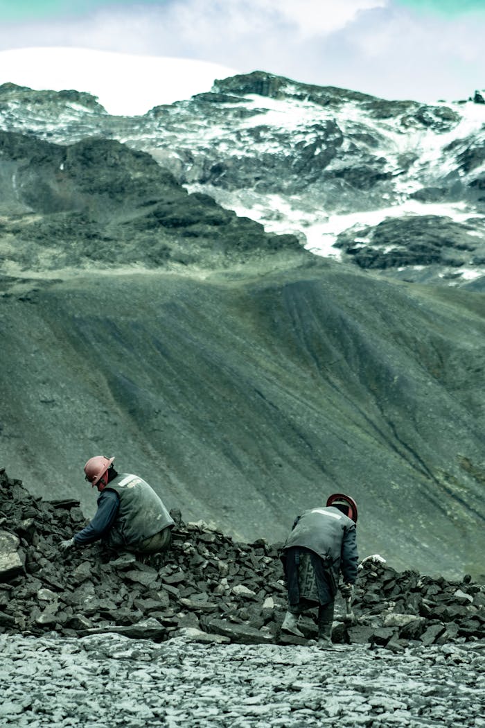 about-03 Two miners in Peru dig through rock piles in the Andes for gold beneath snowy mountains.